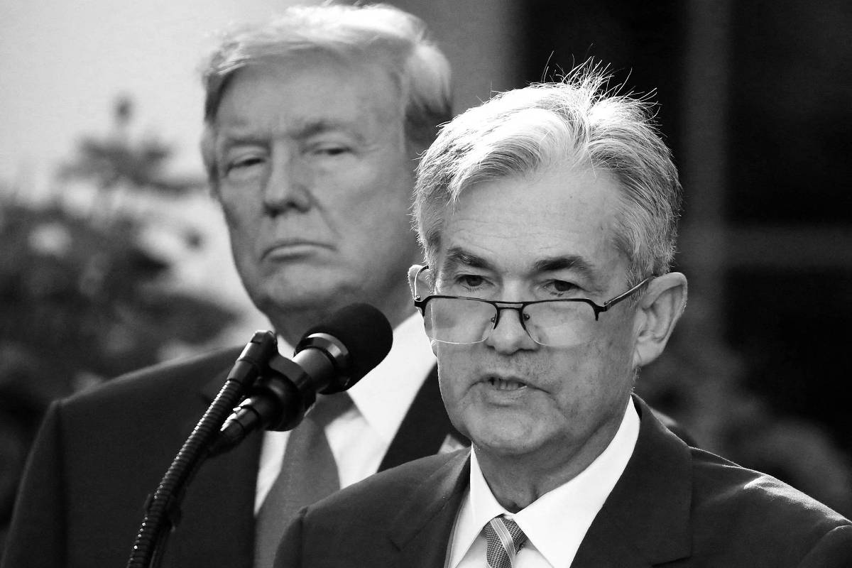 A imagem mostra um evento oficial ao ar livre, onde um homem de cabelo grisalho e óculos está falando ao microfone. Ele usa um terno escuro e uma gravata clara. Ao fundo, um homem com cabelo loiro e uma expressão séria observa. O ambiente é bem iluminado, com vegetação visível ao redor.