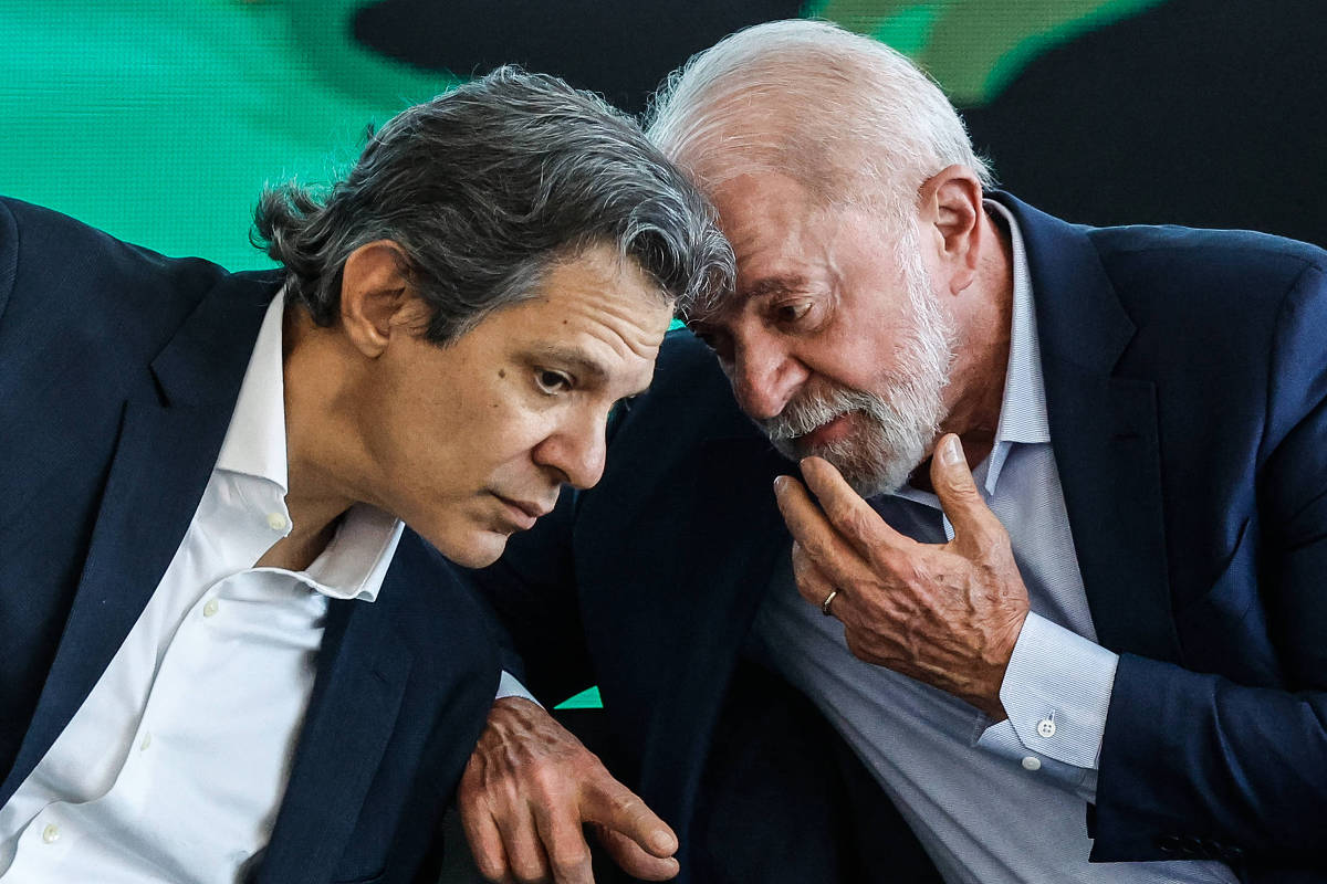 A imagem mostra dois homens sentados próximos um do outro, inclinando-se para frente em uma conversa íntima. O homem à esquerda tem cabelo castanho e usa uma camisa branca com um paletó escuro. O homem à direita tem cabelo grisalho e uma barba curta, também vestindo um paletó escuro. O fundo é desfocado, mas apresenta tons de verde.