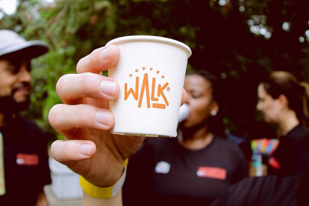 Mão em primeiro plano segura copo branco com logo laranja