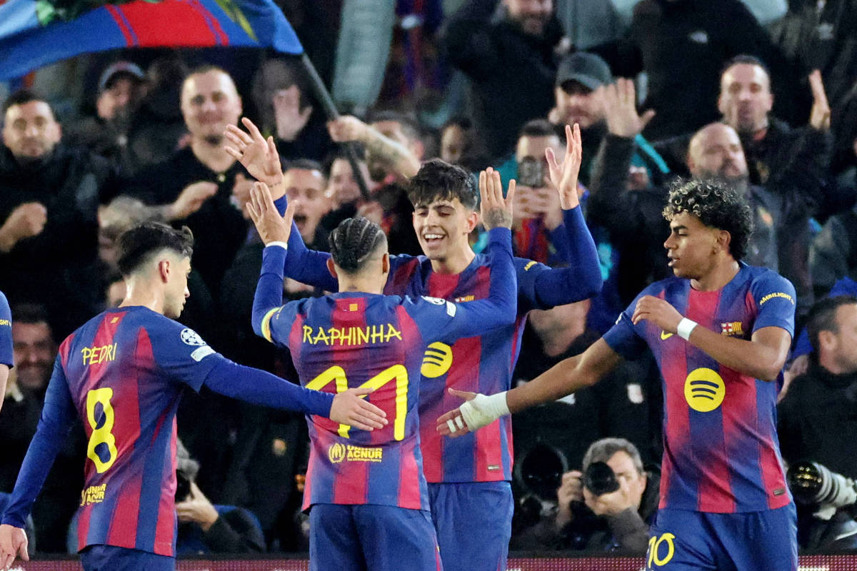 Quatro jogadores do Barcelona em uniforme azul e grená comemoram com mãos levantadas e sorrisos, enquanto torcedores aplaudem ao fundo.
