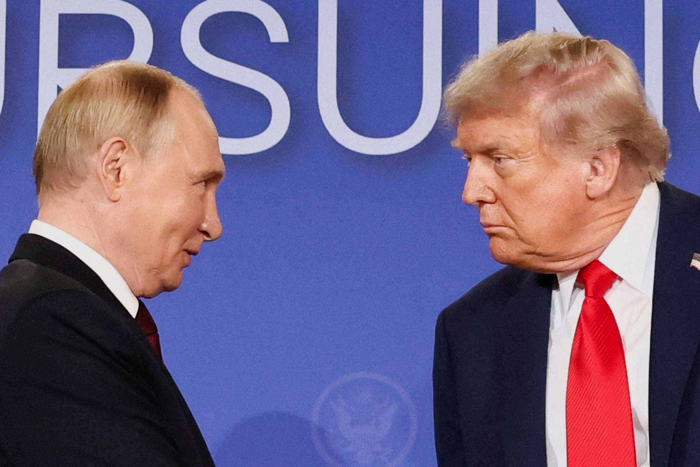 A imagem mostra dois homens em um encontro, um deles com cabelo claro e terno escuro, e o outro com cabelo mais escuro e terno claro. Eles estão se olhando de forma intensa, com um fundo azul e texto em destaque que diz