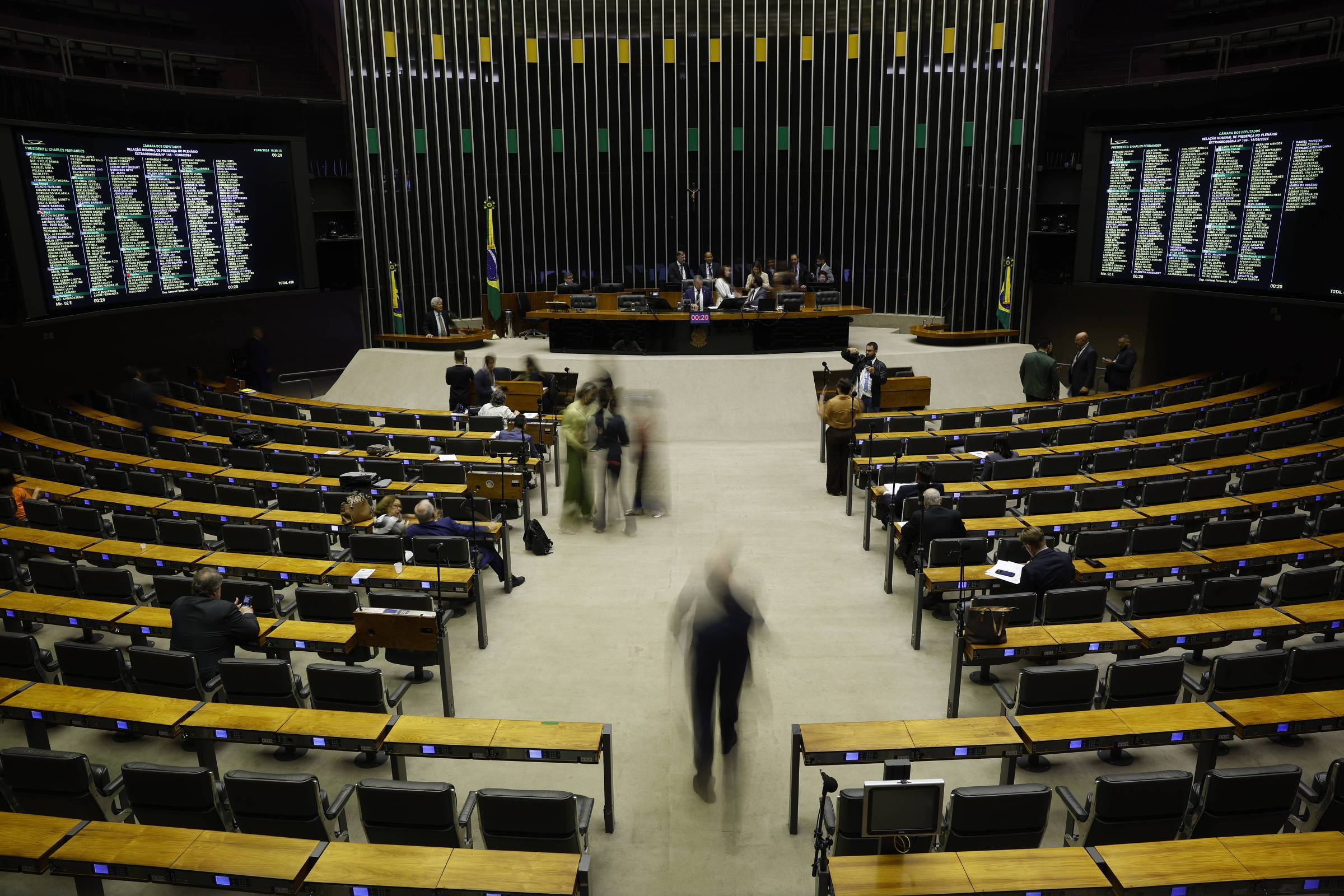 Vista de um plenário com bancadas de madeira, com pessoas se movimentando enter elas. Ao fundo, uma mesa de direção. Aos lados, painéis eletrônicos para registrar o voto de deputados